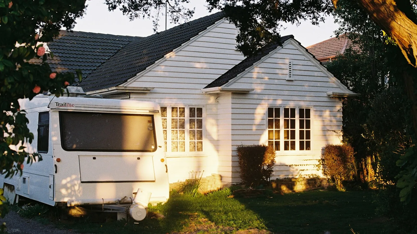 A caravan parked in the driveway of a New Zealand weatherboard bungalow at golden hour
