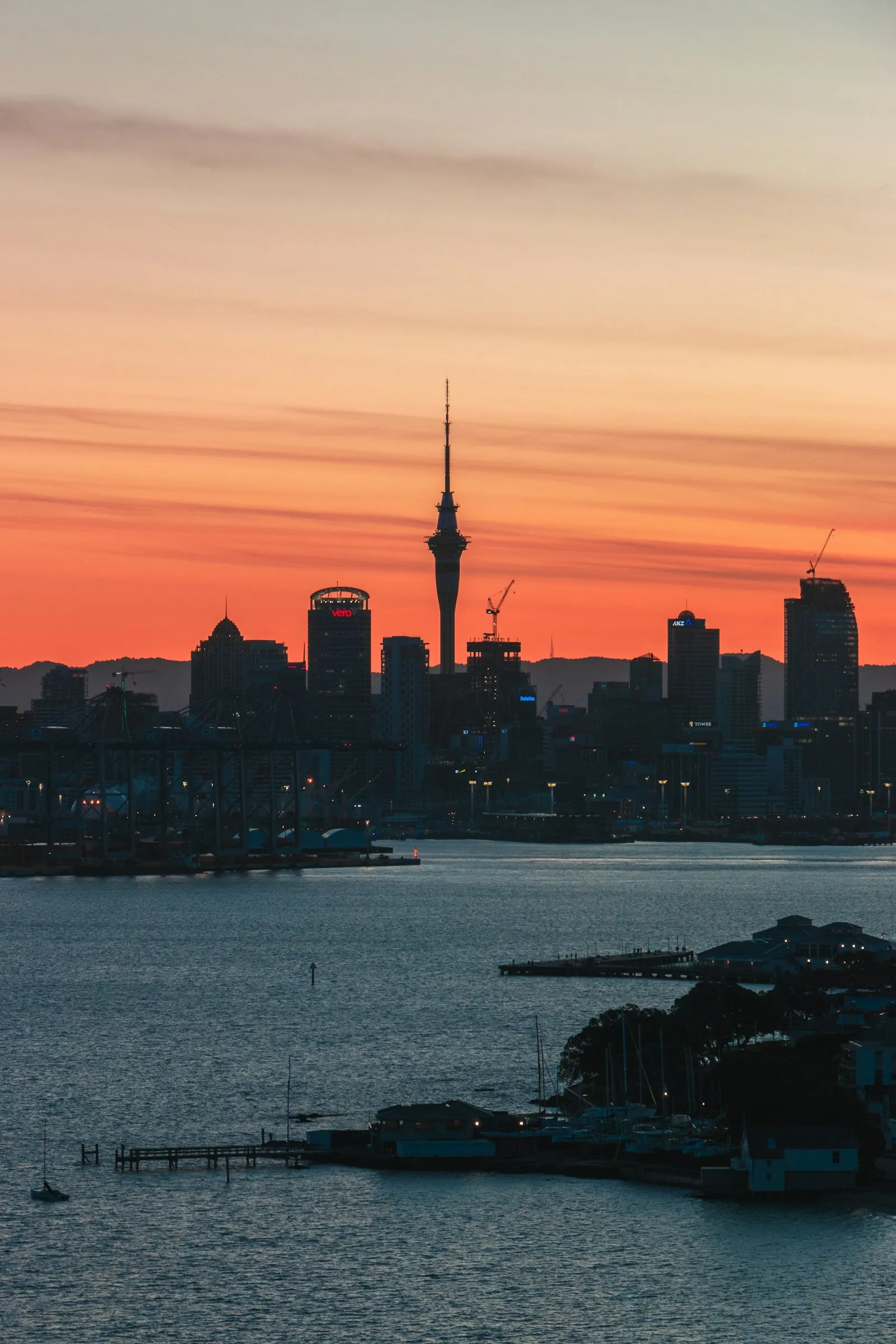 Auckland skyline and harbour silhouetted against a sunset sky, viewed from across the water