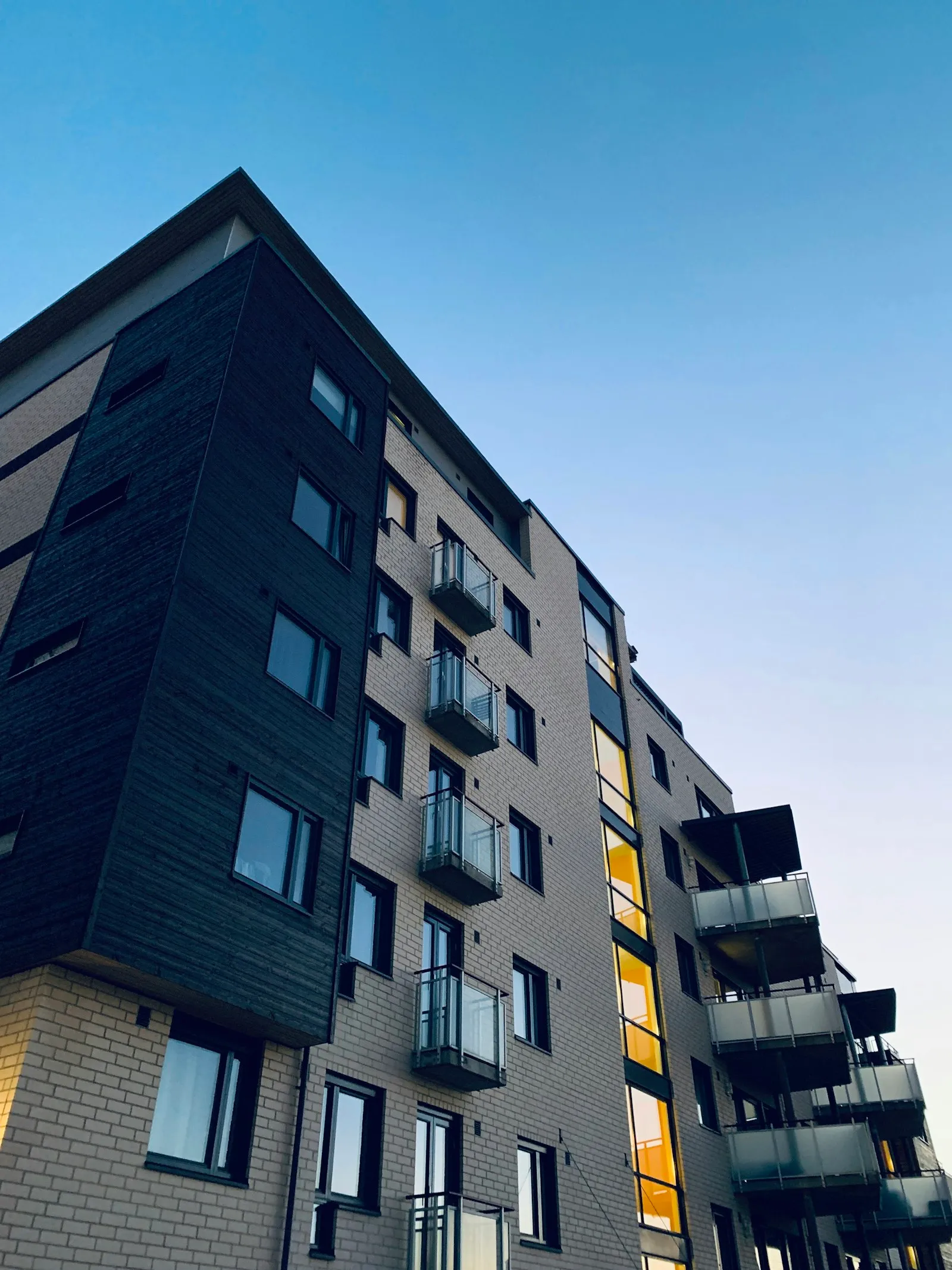 A modern multi-storey apartment building with dark cladding and balconies against a clear blue sky