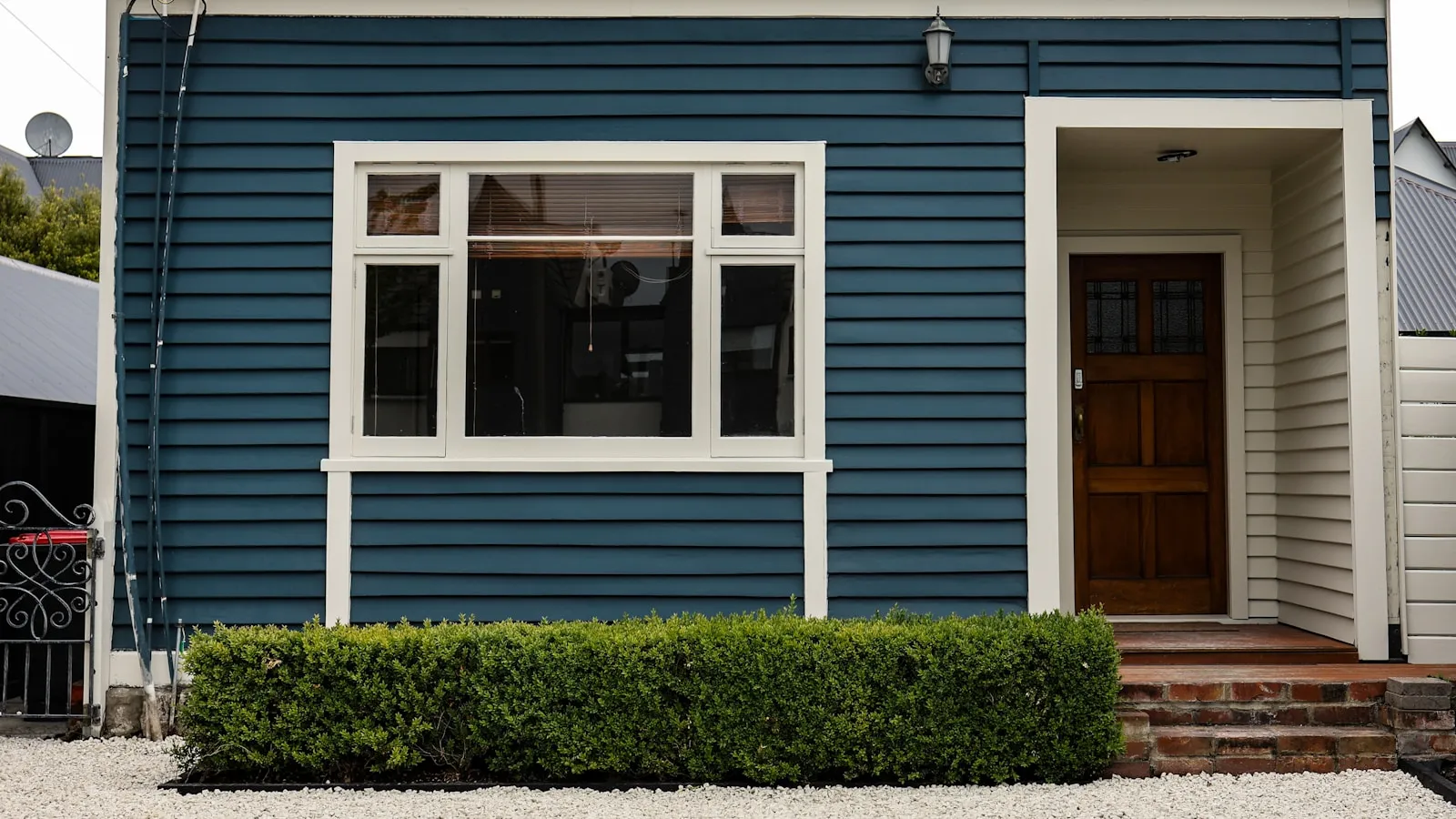 The plain weatherboard front of a single New Zealand house, tidy hedge and front door